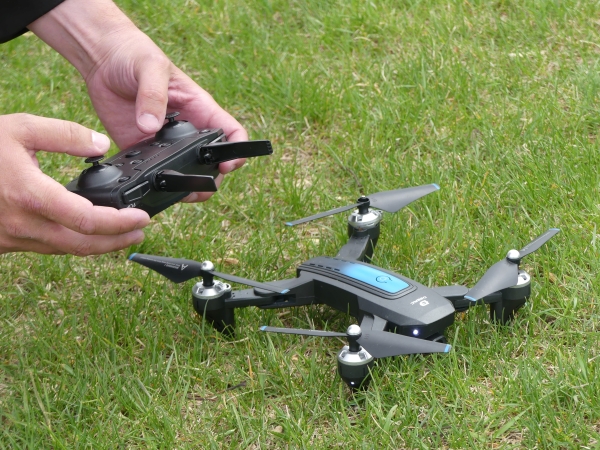 A hand holding a drone controller beside a drone that is laid on grass