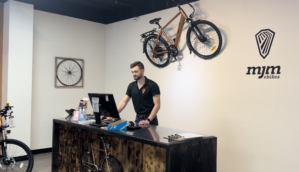 Employee at MJM EBikes working at a desk on a computer with a bike mounted onto the wall behind.